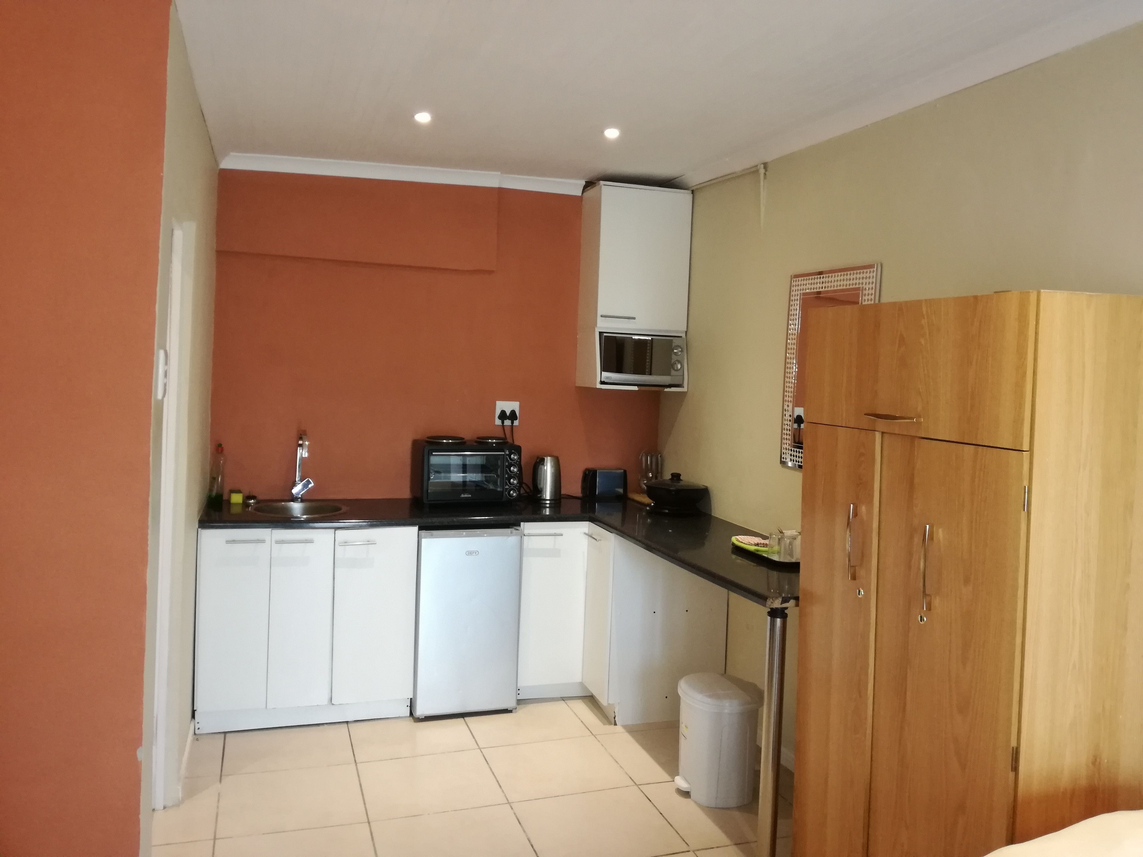 A compact kitchen with white cabinets, a microwave, a toaster, and a small refrigerator.