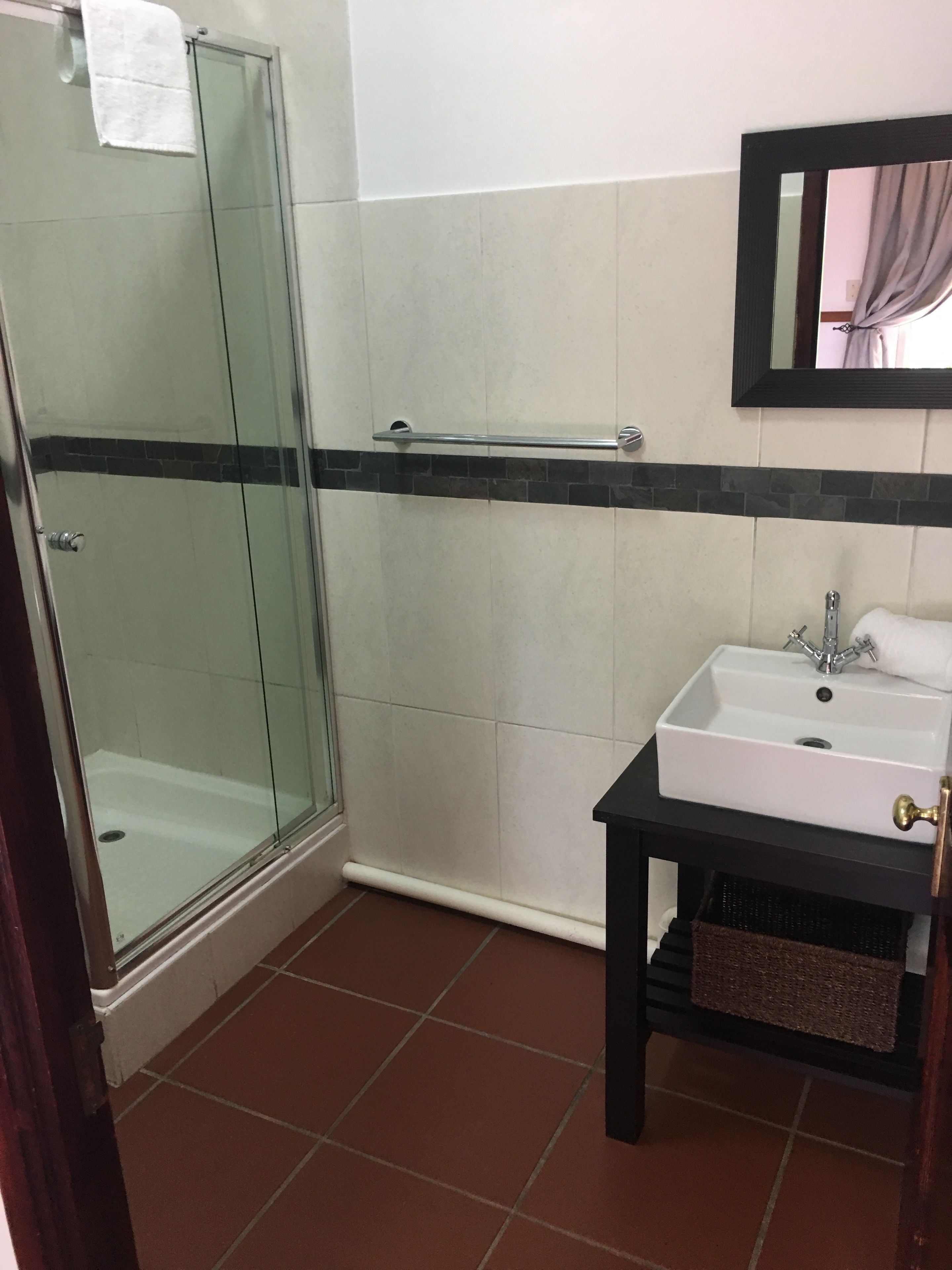Ein Badezimmer mit Glasdusche, einem weißen Waschbecken mit schwarzer Arbeitsplatte und einem Spiegel darüber.