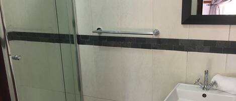 Ein Badezimmer mit Glasdusche, einem weißen Waschbecken mit schwarzer Arbeitsplatte und einem Spiegel darüber.