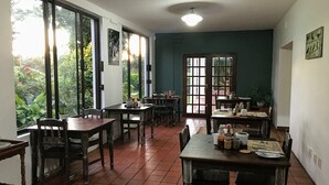 Comedor con mesas y sillas de madera, ventanas amplias con vista a zonas verdes y una lámpara en el techo.