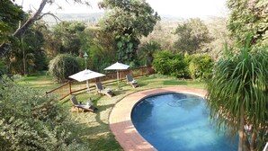 Una piscina con borde de ladrillo, rodeada por una terraza de madera y sillas de descanso.