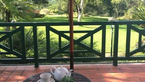 Un patio con una mesa lista para el té, rodeado de una cerca verde y abundante vegetación al fondo.