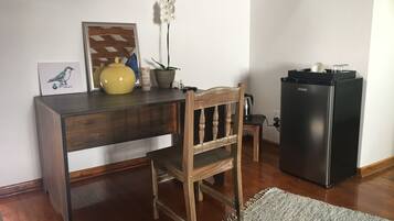 Un escritorio de madera con una silla, un refrigerador negro, una planta en maceta y un cuadro en la pared.