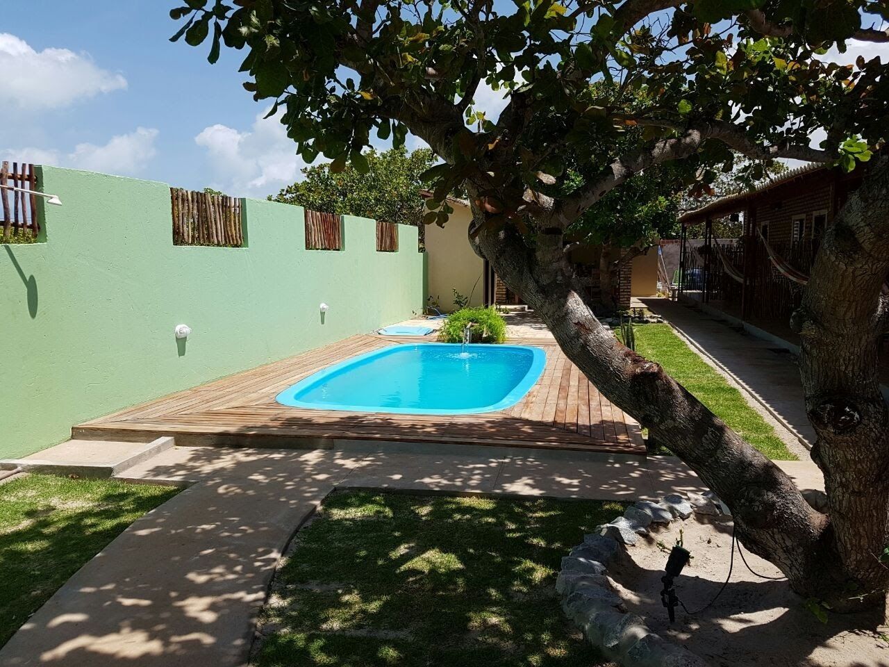 A backyard with a swimming pool, a wooden deck, and a tree.