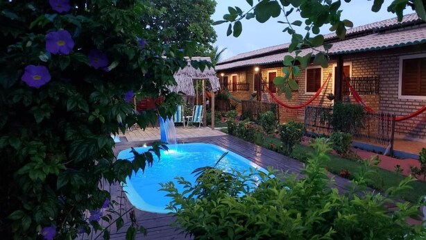 Un área de piscina con una estructura de techo de paja, un edificio de ladrillo con techo de tejas y una barrera de cuerda roja.