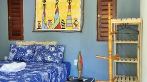 Un dormitorio con una cama, aire acondicionado instalado en la pared, un cuadro colorido y una estantería de madera.