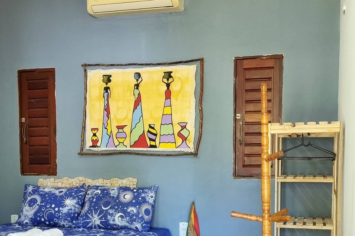 Een slaapkamer met een bed, een wandairconditioner, een kleurrijk schilderij en een houten plankunit.