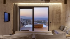 A modern hotel room with a large bed, a sofa, and a balcony with a city view. - North Santorini - A Luxury Spa Hotel (Santorini)