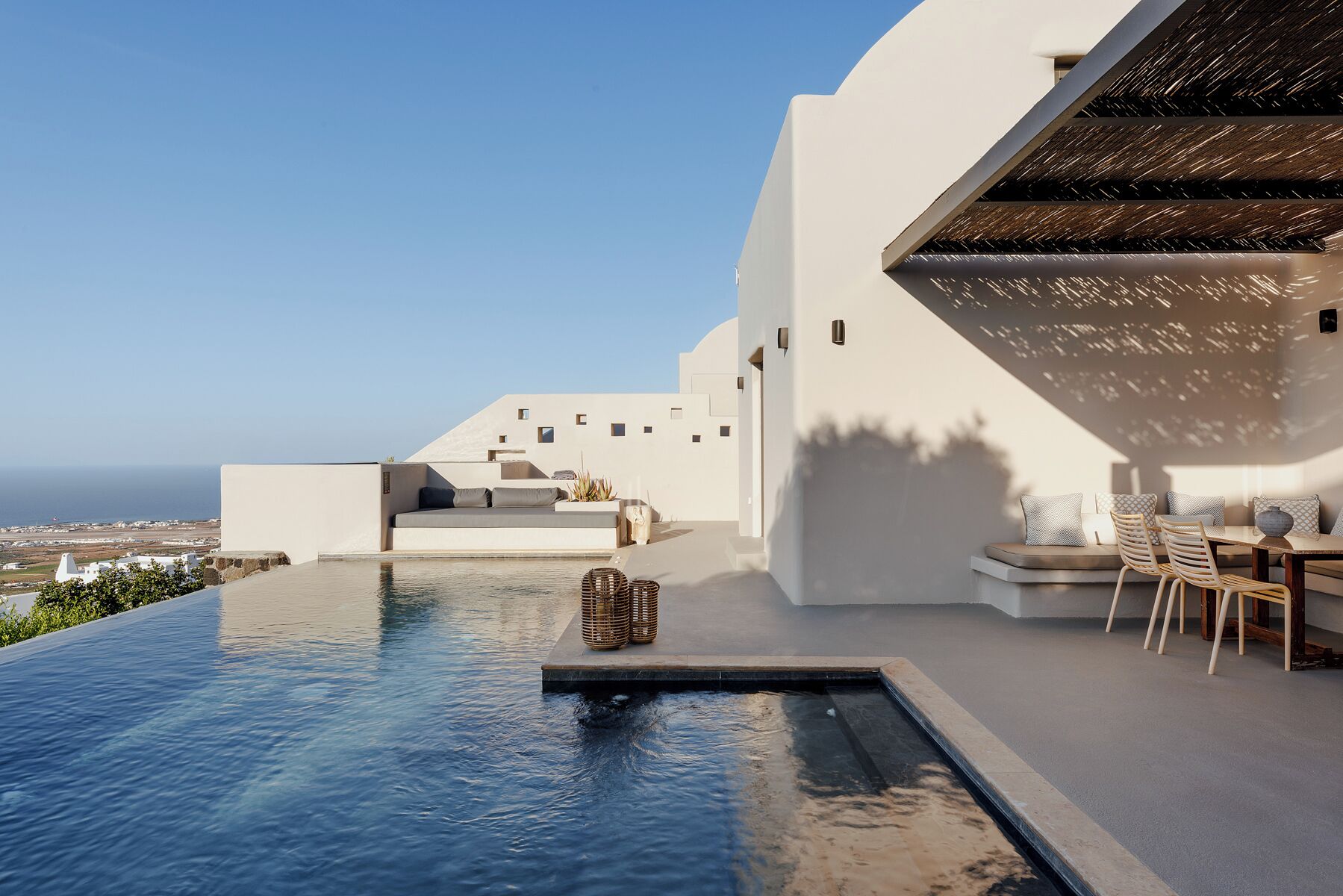 Un espace piscine extérieur moderne avec vue sur la mer, un coin salon agrémenté de coussins et une pergola offrant de l’ombre.