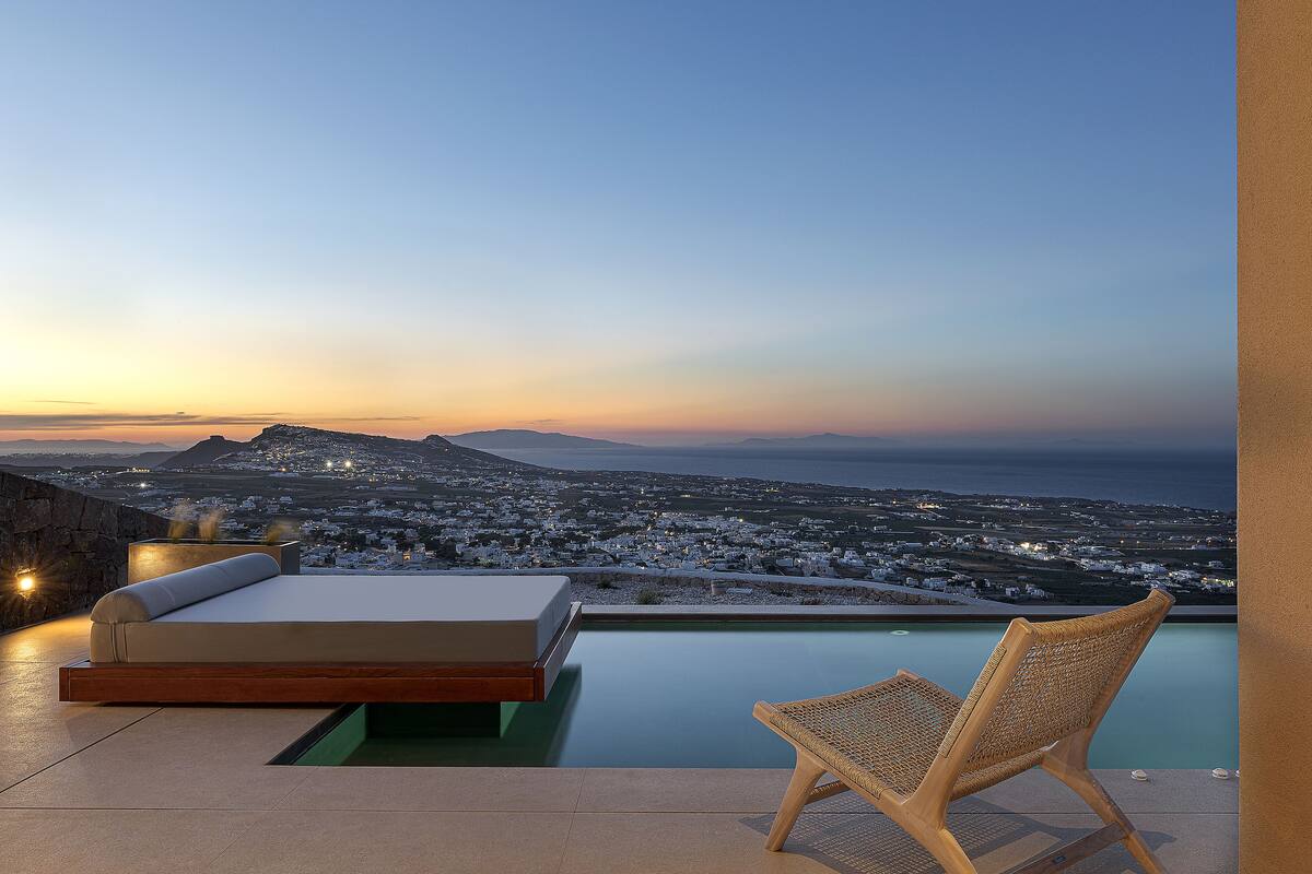 A modern outdoor seating area with a pool, overlooking a coastal cityscape at dusk.