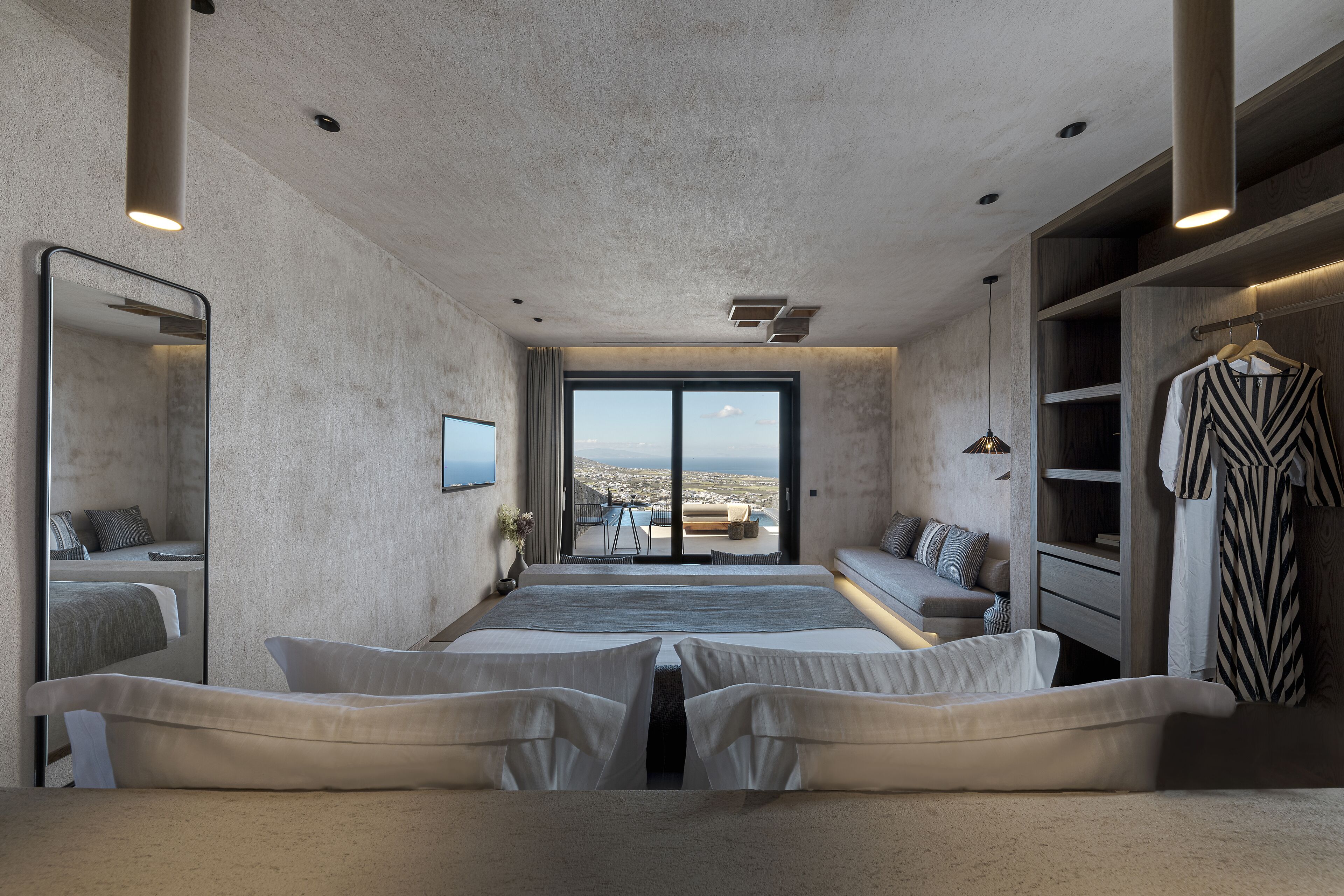 A modern hotel room with a large bed, a seating area, a wardrobe, and a view of the city.