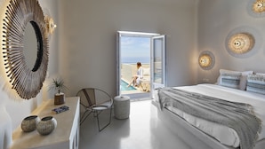 A bedroom with a large bed, a view of the sea through an open door, a round mirror, and a small table with decorative items. - North Santorini - A Luxury Spa Hotel (Santorini)