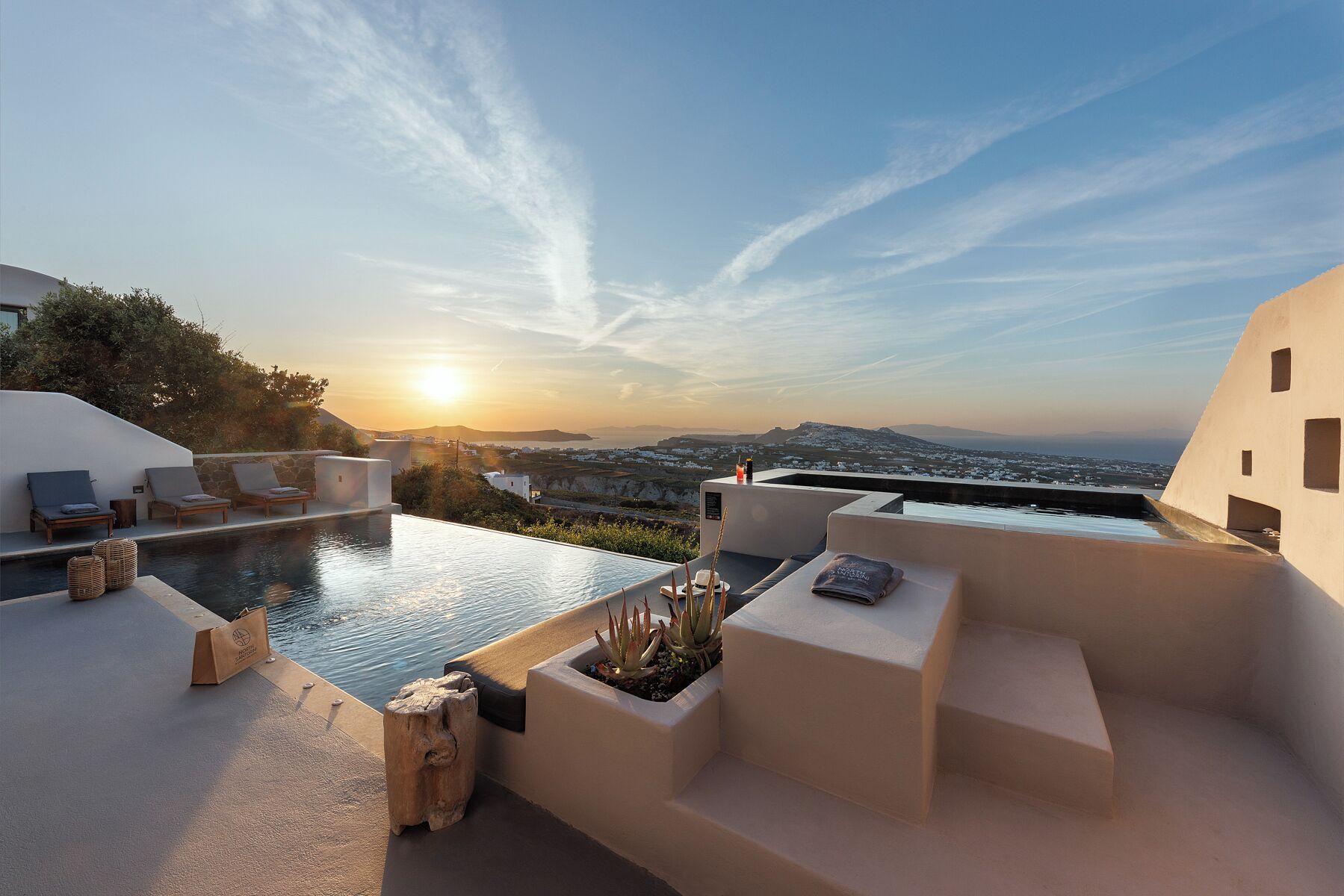 Une piscine à débordement située sur le toit, avec des chaises longues et une vue sur le coucher de soleil surplombant un paysage côtier.