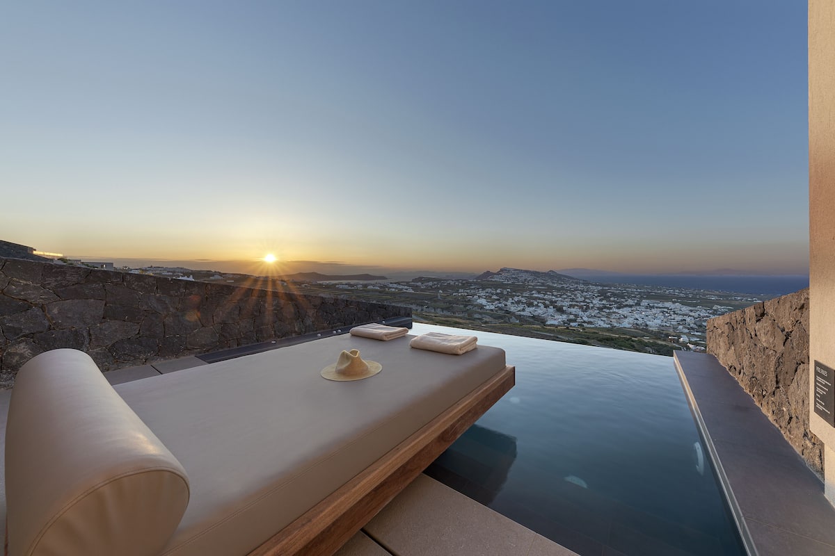 A sunlit infinity pool with a view of a snowy landscape and a sunset.