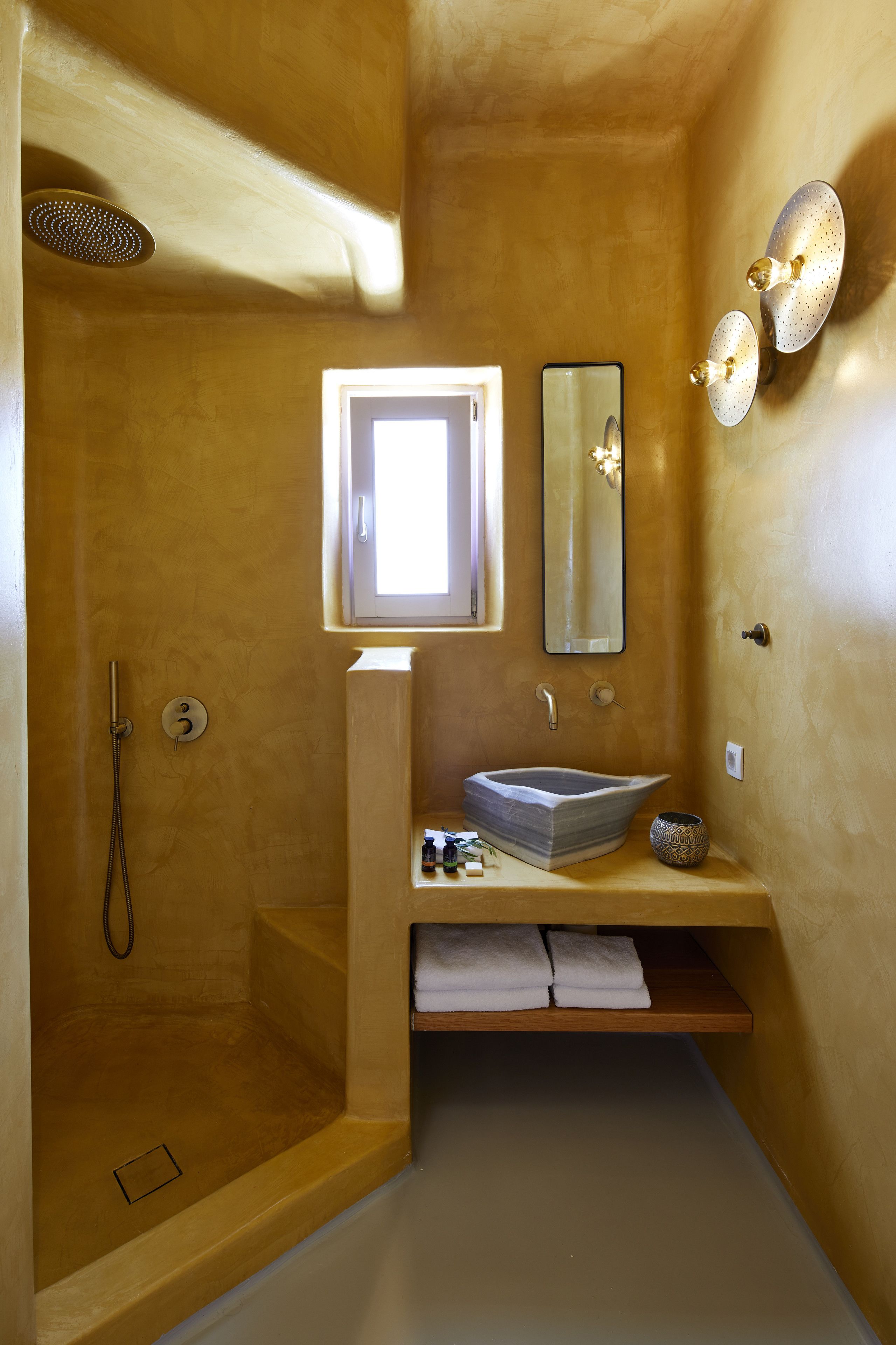 A bathroom with a walk-in shower, a sink with a vessel basin, a mirror, and a shelf with towels.