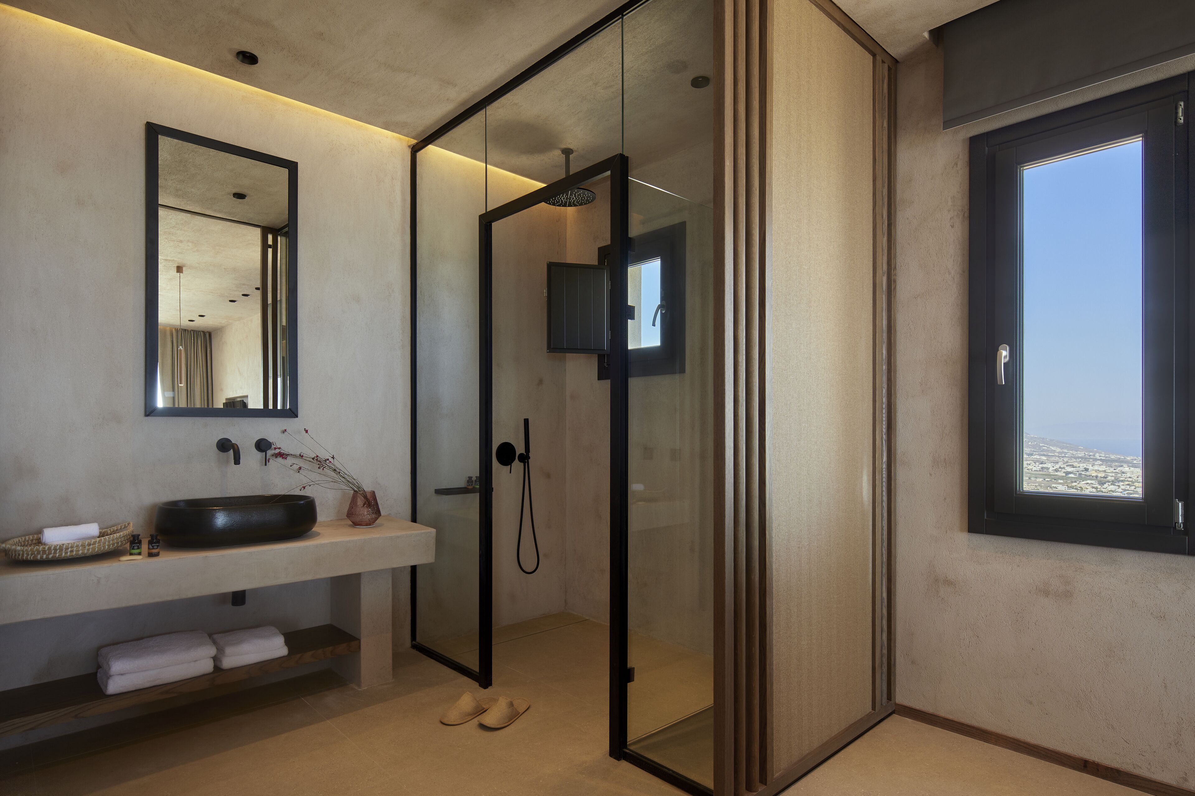 Une salle de bain moderne avec une douche à parois de verre, un grand miroir, un lavabo avec un receveur et une fenêtre offrant une belle vue.
