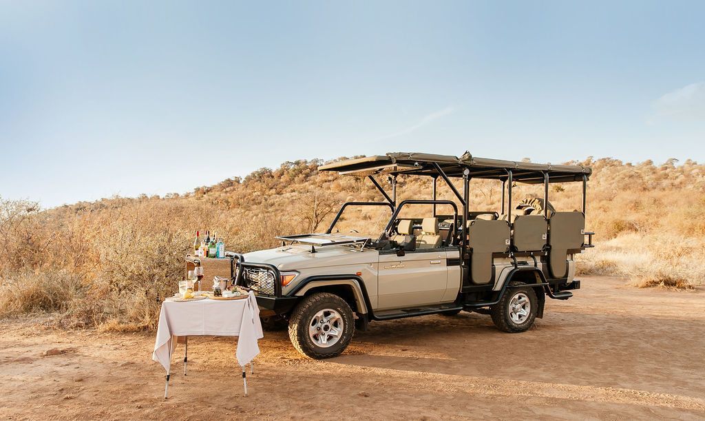 Un vehículo safari con una mesa dispuesta en una zona seca y cubierta de hierba.