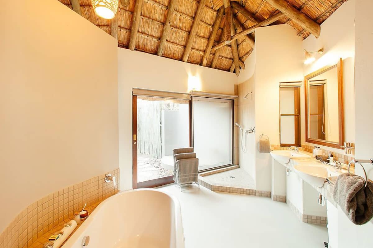Une salle de bain avec une grande baignoire, une douche et un lavabo double. Il y a une fenêtre donnant sur l’extérieur.