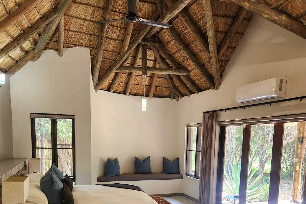 Une chambre à coucher comprenant un lit, une table de chevet, une fenêtre, un ventilateur de plafond et une grande baie vitrée donnant sur un paysage verdoyant.