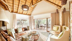 Ein geräumiges Wohnzimmer mit hoher Decke, Ledersofas, einem Glastisch und einem Essbereich, der durch große Fenster sichtbar ist.