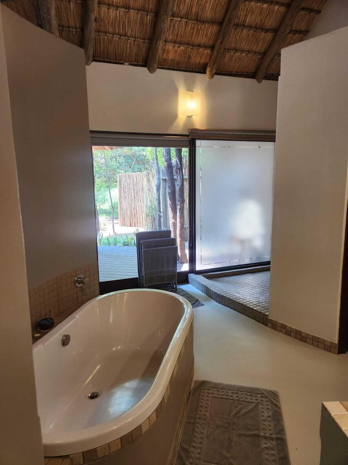 Un baño con una bañera grande, ducha y puerta de vidrio que da a un espacio exterior.