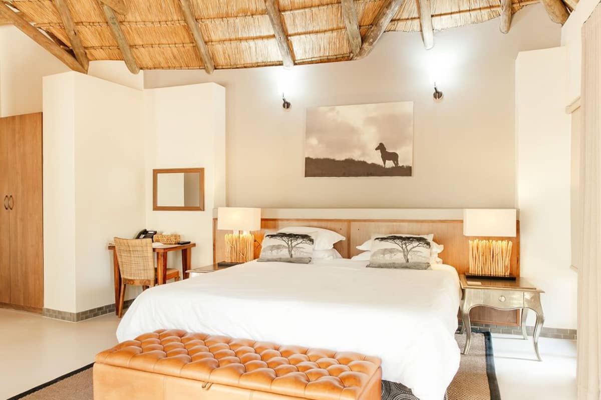 Une chambre d’hôtel avec un grand lit, un bureau avec une chaise, une petite table, un miroir et un tableau au mur.
