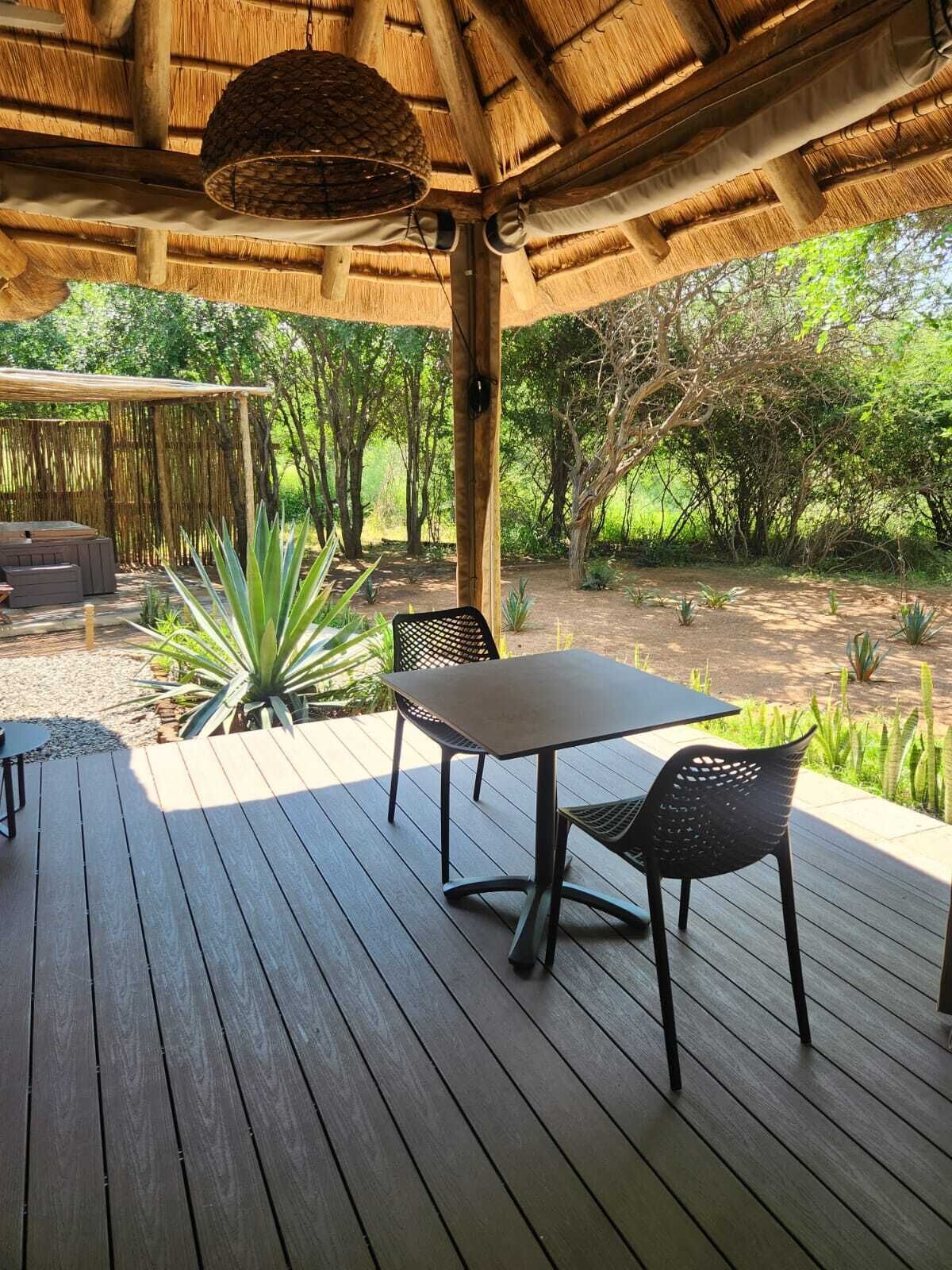 Une terrasse en bois avec une table et des chaises, entourée d’une végétation luxuriante et d’arbres.