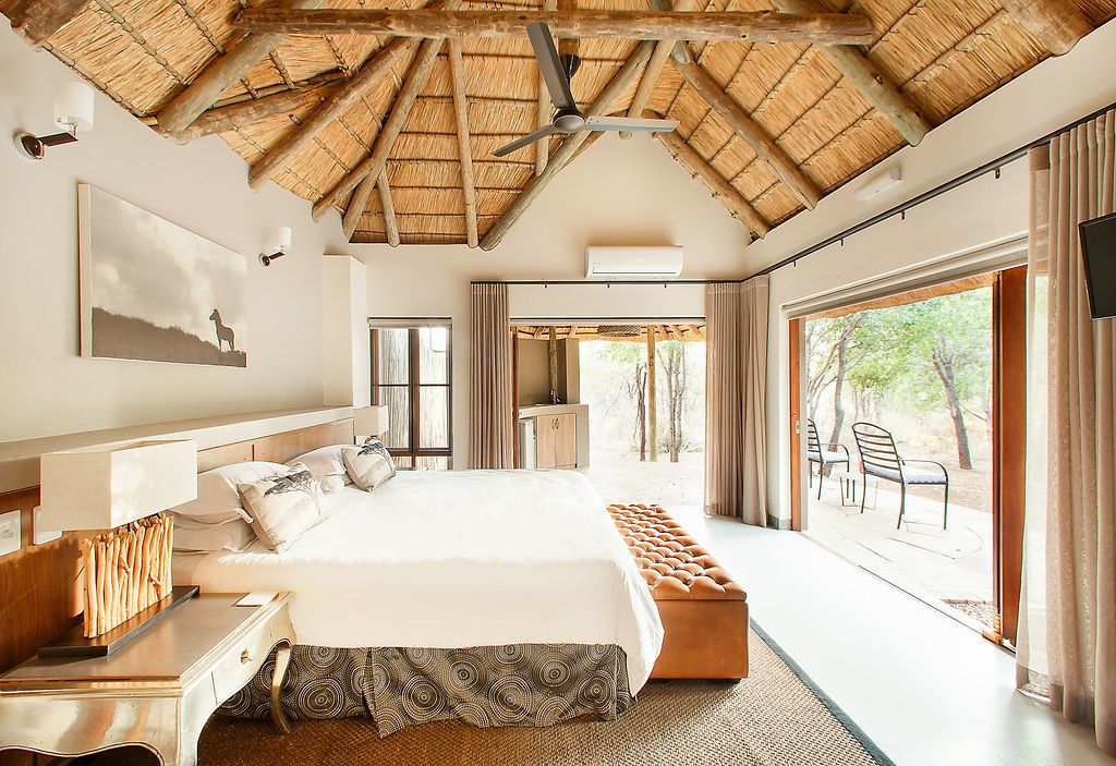 Une chambre spacieuse avec un grand lit, une tête de lit en bois, un ventilateur de plafond et une vue sur l’extérieur grâce à une porte-fenêtre coulissante.