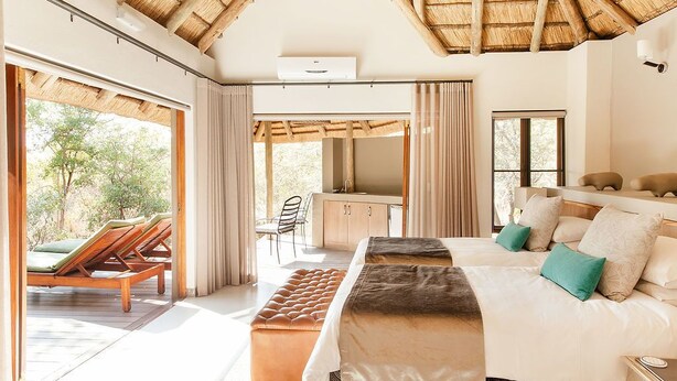 Ein geräumiges Schlafzimmer mit einem großen Bett, einem Schreibtisch und einem Stuhl, verbunden mit einem Balkon mit Liegestühlen.