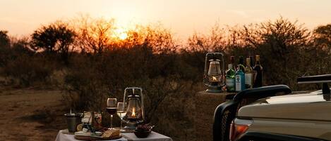 A table set outdoors with food, drinks, and a lantern against a sunset backdrop.