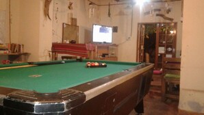 A pool table with balls, a television, and a red cloth.