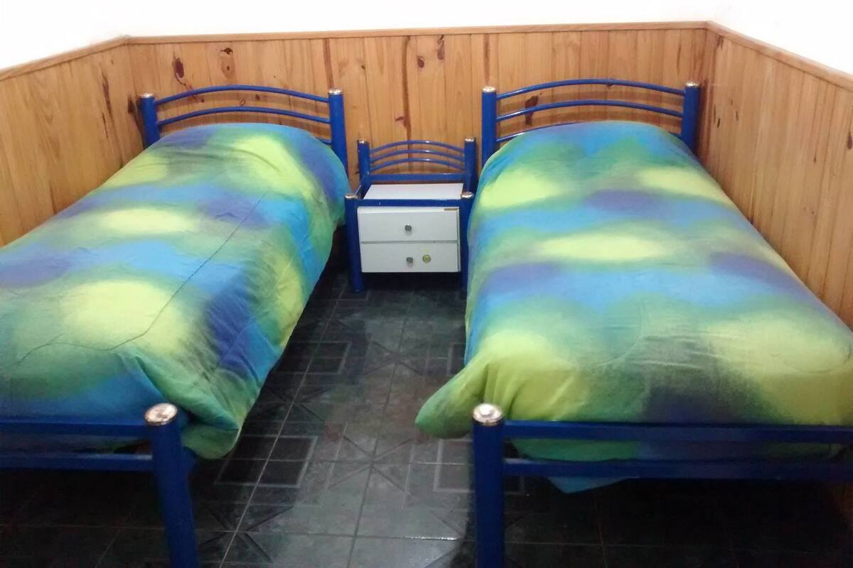 Ein Zimmer mit zwei Einzelbetten, einem kleinen Nachttisch und einer Holzwand.