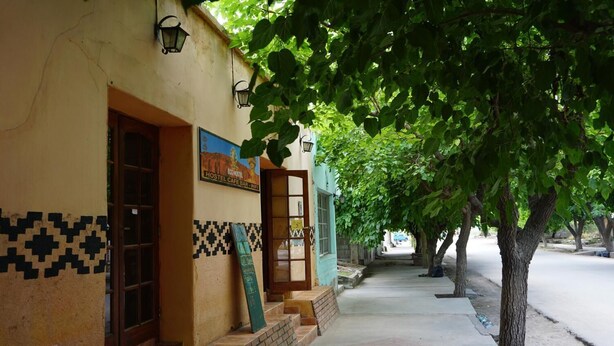A hostel with a tiled facade, a signboard, and a pathway lined with trees.
