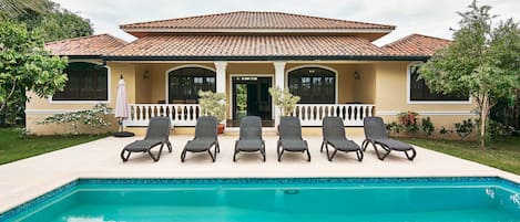 Una casa con piscina, cinco sillas de descanso y techo de tejas.