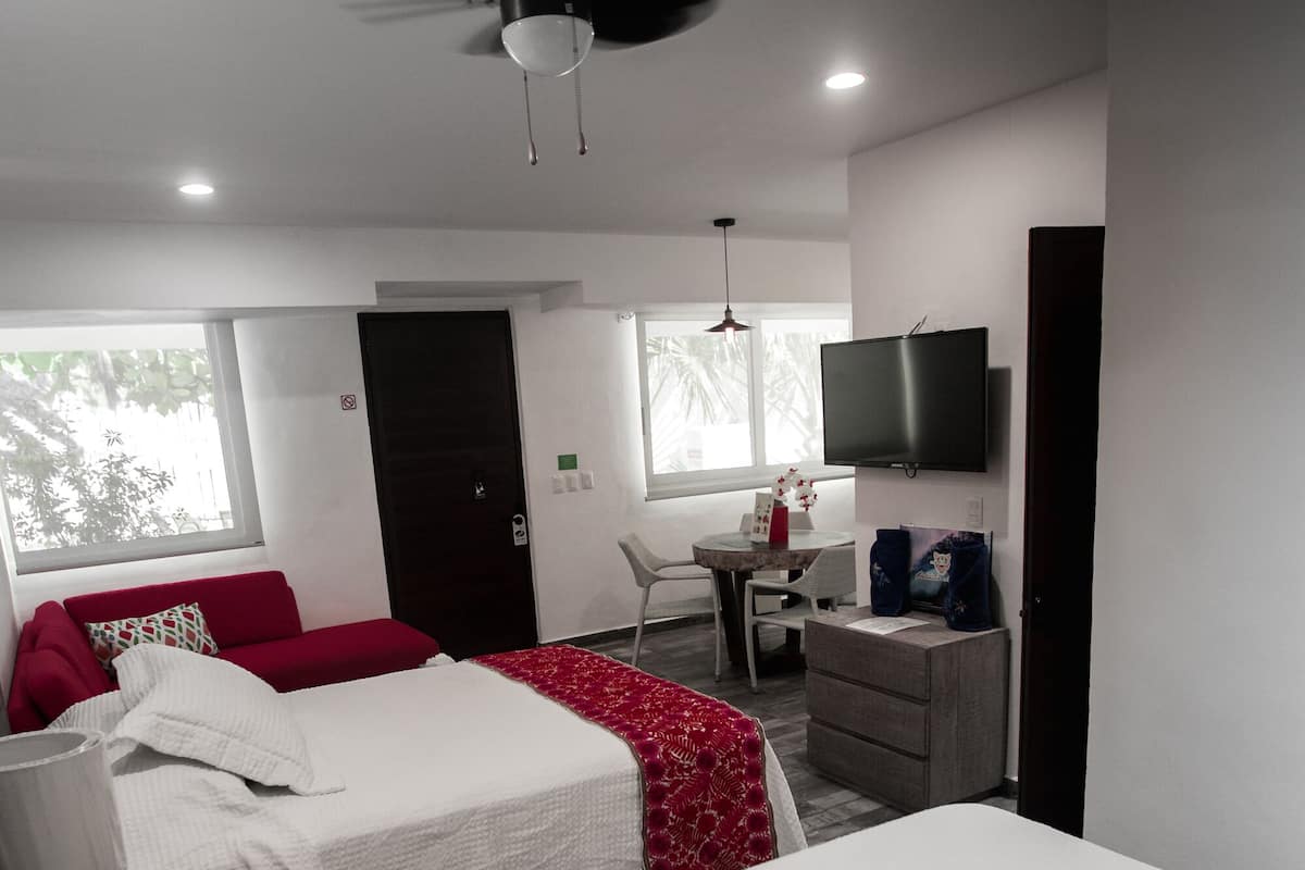 A hotel room with two beds, a desk, a chair, a TV, and a ceiling fan.