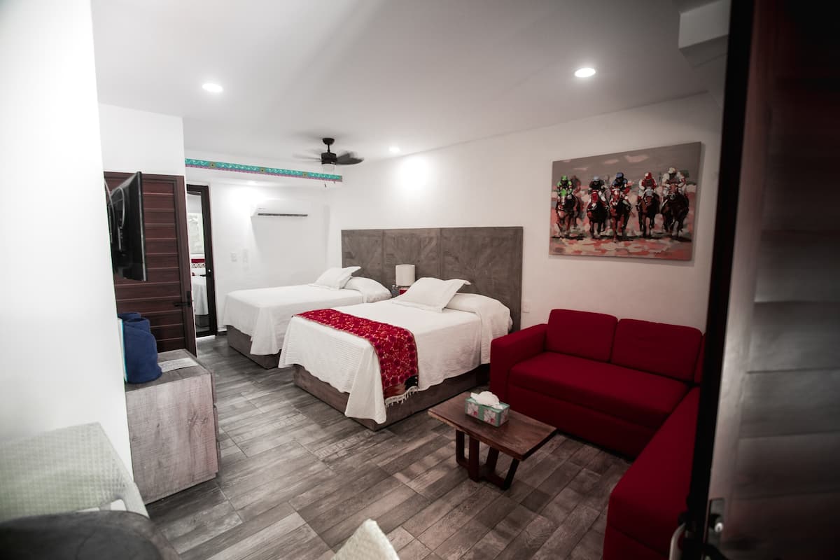 A hotel room with two beds, a red sofa, a small table, and a painting on the wall.