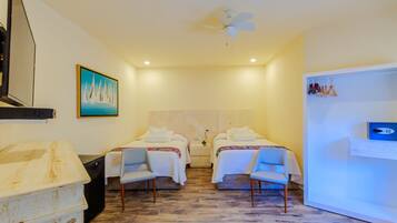 Une chambre d’hôtel avec deux lits, un ventilateur de plafond, un tableau, un bureau avec un ordinateur et un mini-bar.