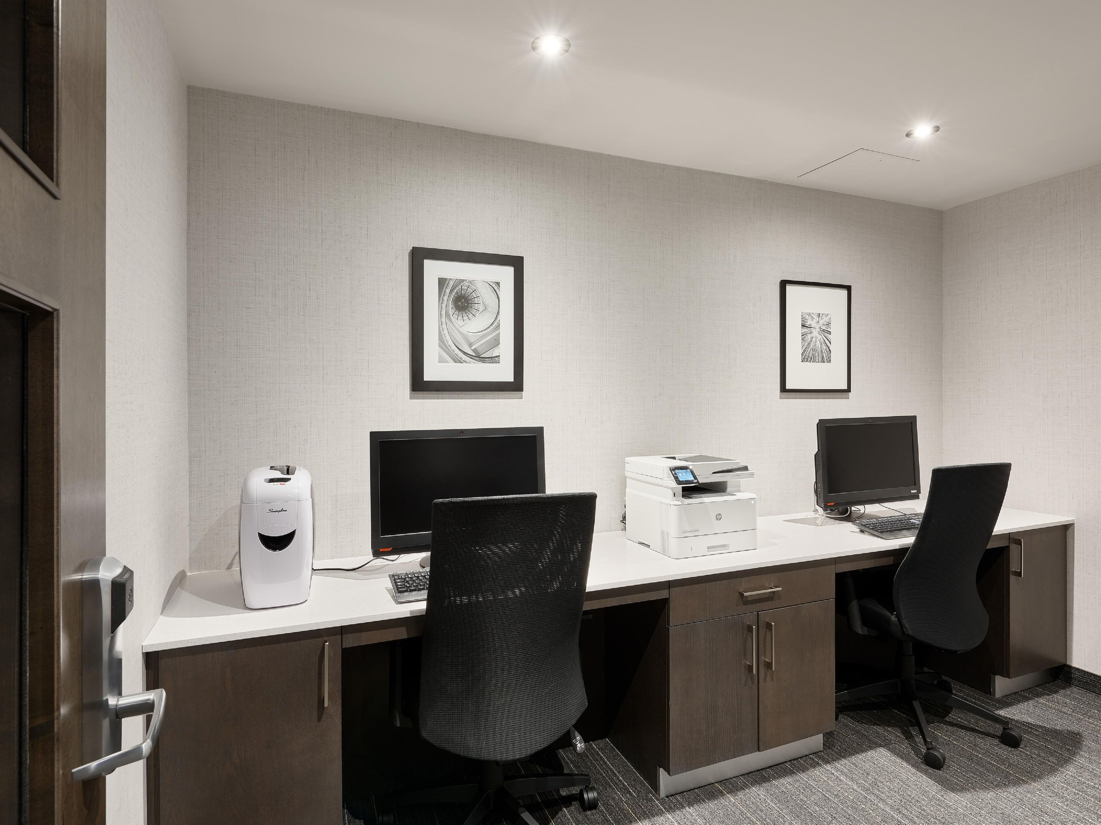 A modern office space with two desks, chairs, computers, and printers.