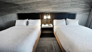 A hotel room with two beds, a dark headboard, a small table with a lamp, and a patterned carpet.