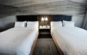 A hotel room with two beds, a dark headboard, a small table with a lamp, and a patterned carpet. - Hampton Inn & Suites by Hilton Quebec City Levis (Levis)