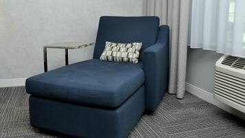Un sillón azul oscuro con un cojín estampado, una mesita auxiliar y una ventana con cortinas de gasa.