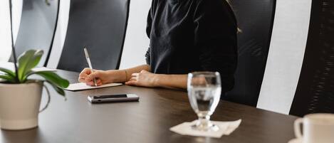 A person sitting at a table with a notebook, pen, smartphone, and a glass of water.