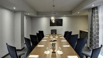 A conference room with a long table, chairs, a projector screen, and a coffee pot.