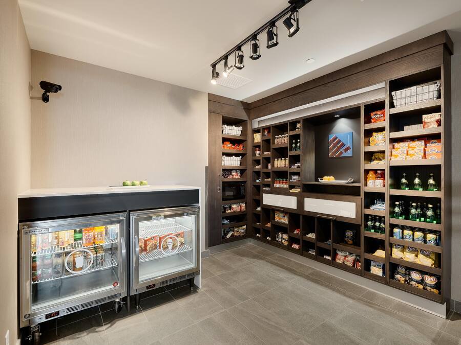 A kitchenette with two beverage air fridges, a microwave, and a variety of snacks and beverages on shelves.
