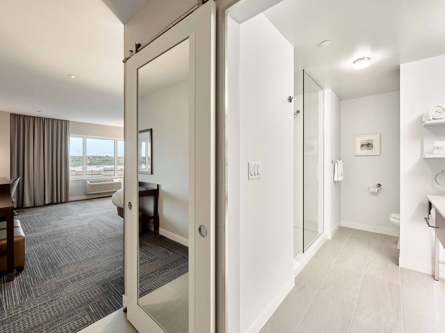 Quarto de hotel com escrivaninha, cama, banheiro com vaso sanitário e pia, e vista para a cidade.