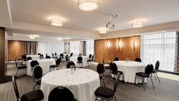 Un salón de conferencias con mesas redondas, sillas negras y manteles blancos.
