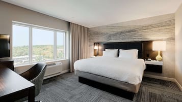 Hotellihuone, jossa on suuri sänky, työpöytä, tuoli, televisio ja näkymä ulos.