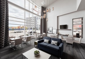 A modern hotel lobby with a large window, a blue sofa, and a dining area. - Hampton Inn & Suites by Hilton Quebec City Levis (Levis)