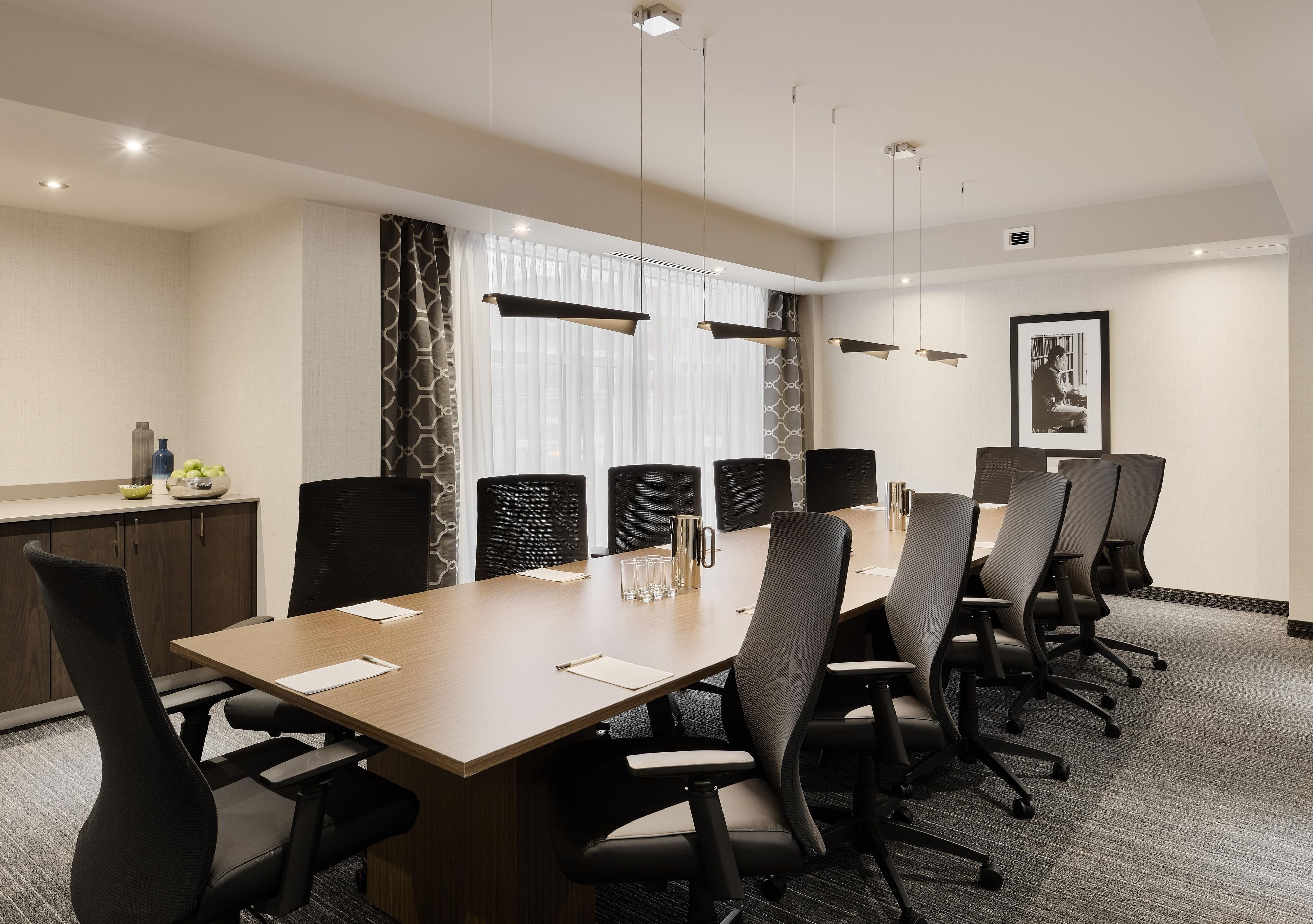 A conference room with a long table, multiple chairs, a whiteboard, and a framed picture on the wall.