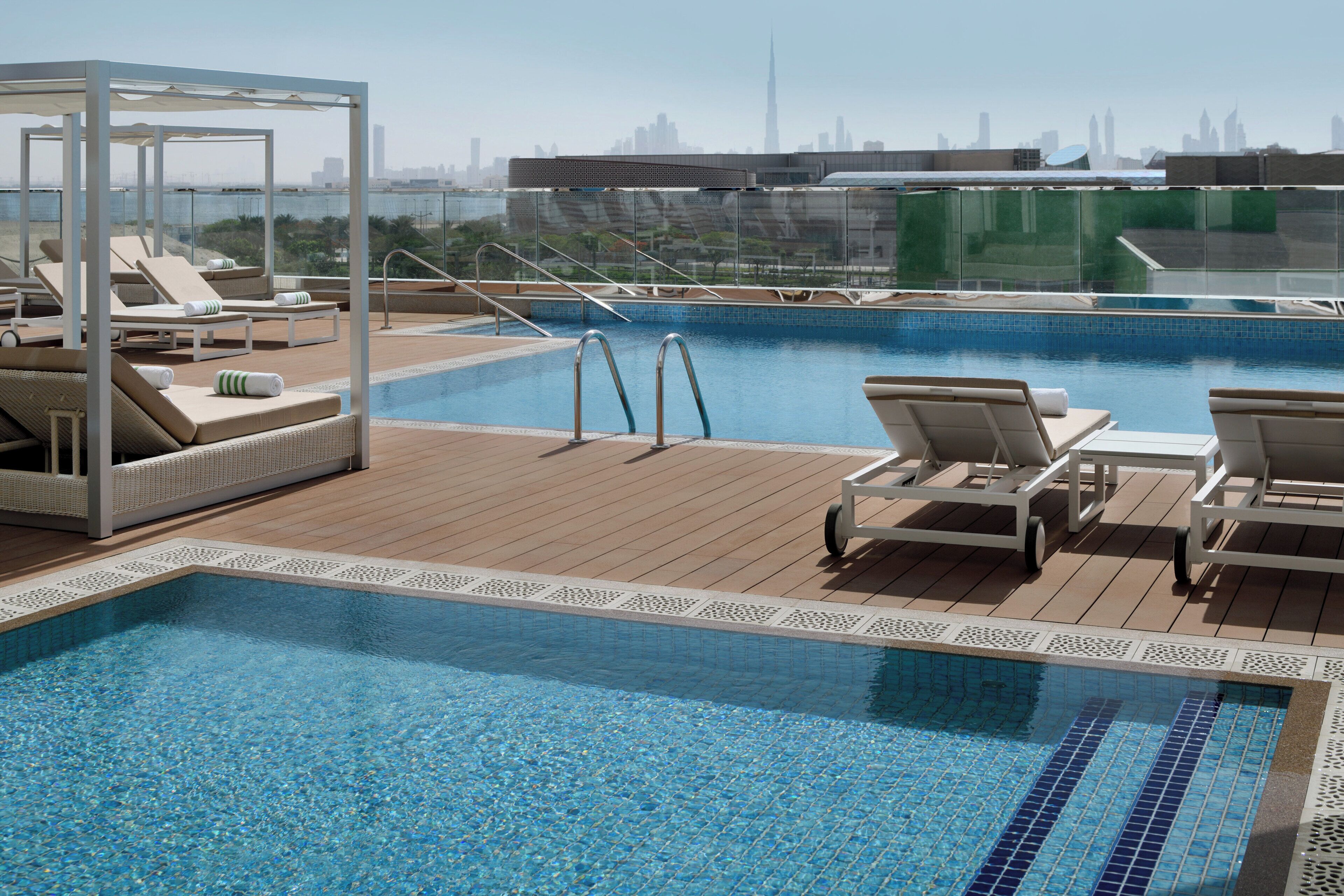 Una piscina en la azotea con sillones de descanso y vistas del horizonte de la ciudad.